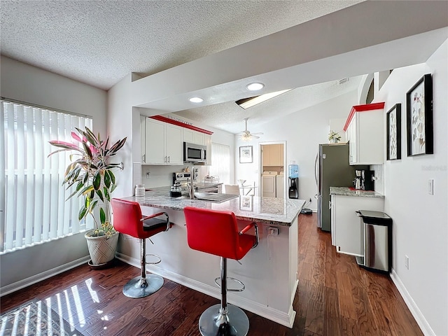 kitchen featuring stainless steel appliances, kitchen peninsula, a breakfast bar area, and white cabinets