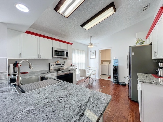 kitchen featuring sink, stainless steel appliances, independent washer and dryer, white cabinets, and vaulted ceiling