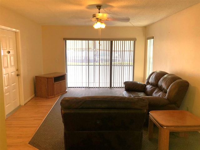 living room featuring ceiling fan, light hardwood / wood-style floors, and a textured ceiling