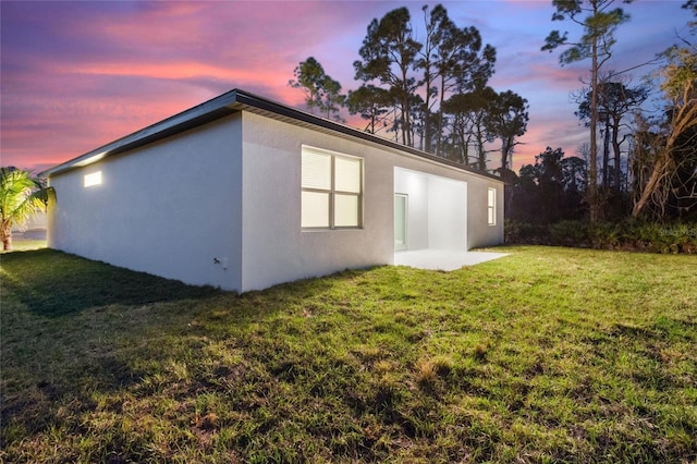 property exterior at dusk with a patio and a yard