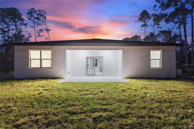 back house at dusk featuring a yard and a patio area