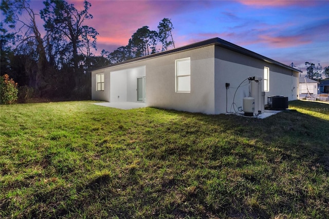 back house at dusk with a patio, a yard, and central AC unit