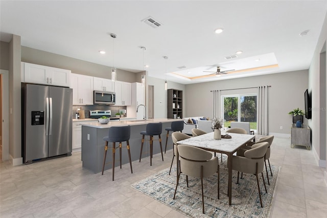 tiled dining room with sink, a tray ceiling, and ceiling fan