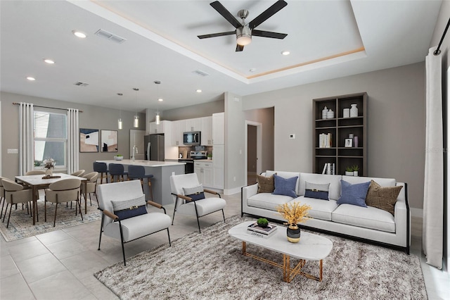 living room with sink, a tray ceiling, light tile patterned floors, and ceiling fan