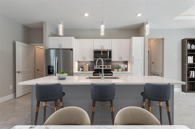 kitchen featuring a kitchen island with sink, decorative light fixtures, white cabinets, and appliances with stainless steel finishes