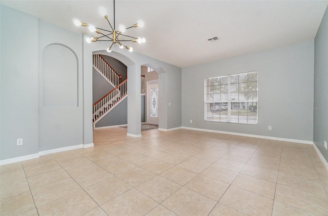 tiled spare room featuring a chandelier