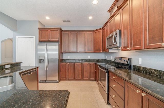 kitchen featuring light tile patterned floors, stainless steel appliances, dark stone counters, and a textured ceiling