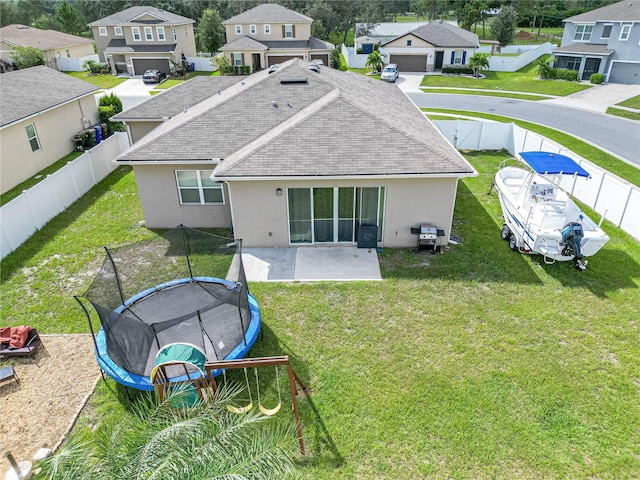 rear view of property with a trampoline, a patio area, and a lawn