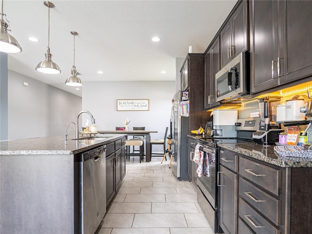 kitchen featuring appliances with stainless steel finishes, sink, dark stone counters, hanging light fixtures, and a kitchen island with sink