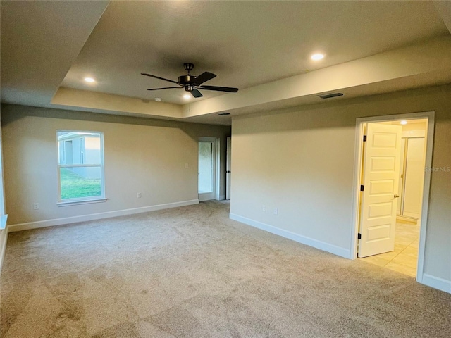 carpeted spare room with ceiling fan and a tray ceiling