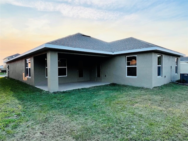 back house at dusk featuring a yard and a patio