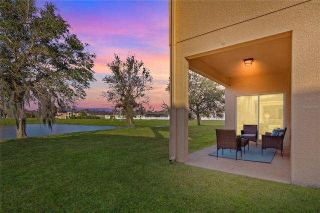 yard at dusk featuring a patio and a water view