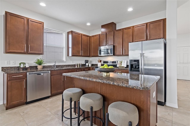 kitchen featuring a kitchen island, sink, dark stone countertops, a kitchen breakfast bar, and stainless steel appliances