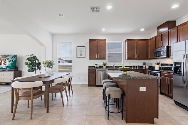 kitchen featuring dark stone countertops, dark brown cabinets, stainless steel appliances, a kitchen breakfast bar, and a kitchen island