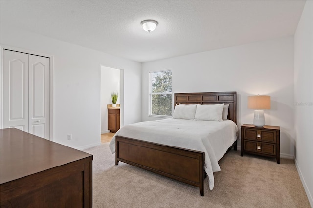 bedroom with ensuite bath, light carpet, a textured ceiling, and a closet