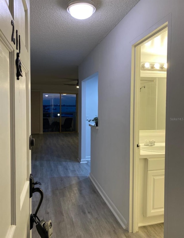 hall with dark wood-type flooring, sink, and a textured ceiling