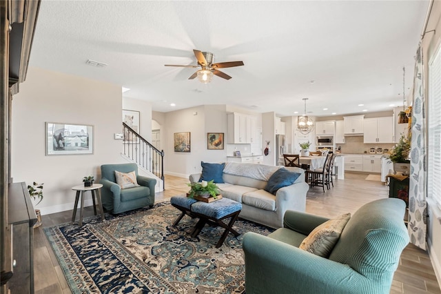 living room featuring ceiling fan with notable chandelier and light hardwood / wood-style flooring