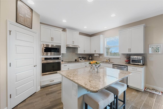 kitchen with a breakfast bar, light stone counters, a center island, appliances with stainless steel finishes, and white cabinets