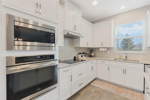 kitchen featuring appliances with stainless steel finishes, white cabinetry, sink, decorative backsplash, and light hardwood / wood-style floors