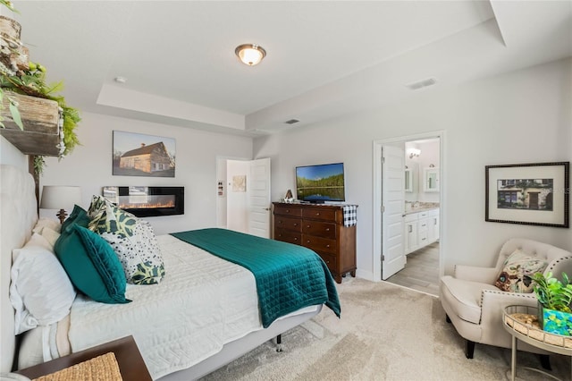 carpeted bedroom with connected bathroom and a raised ceiling