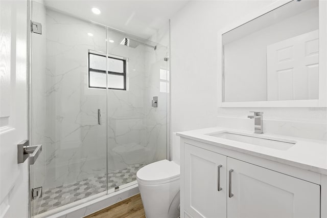 bathroom featuring wood-type flooring, toilet, vanity, and a shower with shower door