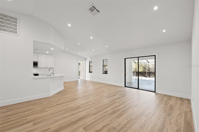 unfurnished living room featuring high vaulted ceiling, sink, and light hardwood / wood-style flooring