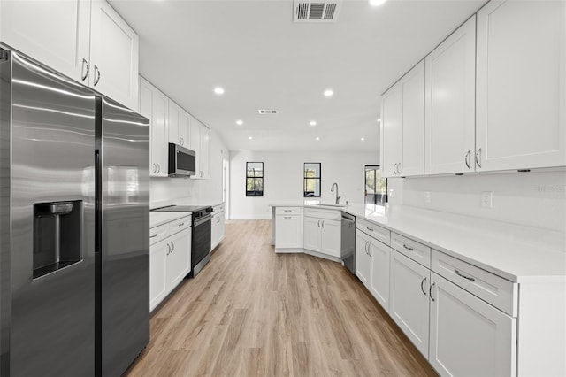 kitchen with sink, light hardwood / wood-style flooring, appliances with stainless steel finishes, white cabinets, and kitchen peninsula