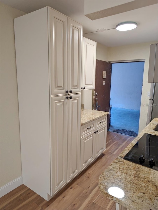 kitchen with stainless steel refrigerator, white cabinetry, light stone countertops, black electric cooktop, and light hardwood / wood-style flooring