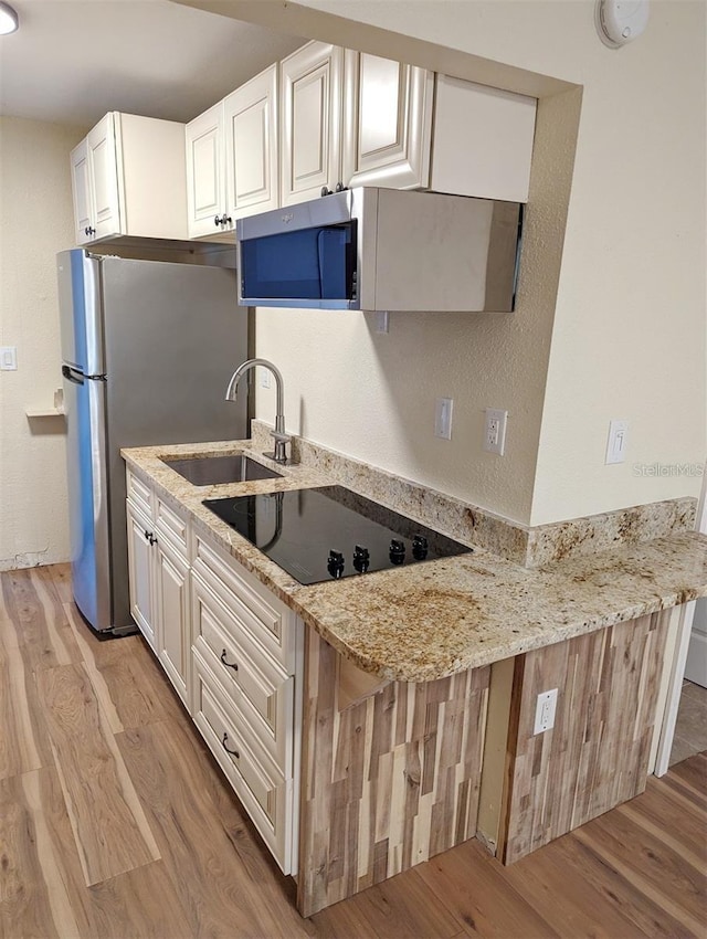 kitchen featuring sink, light stone counters, light hardwood / wood-style flooring, black electric stovetop, and white cabinets