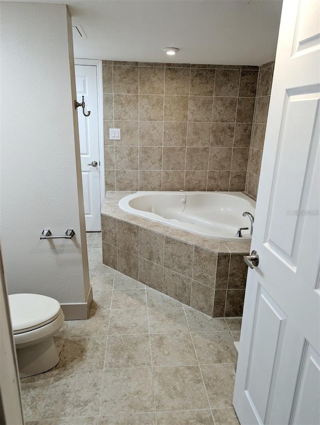 bathroom featuring tile patterned flooring, a relaxing tiled tub, and toilet