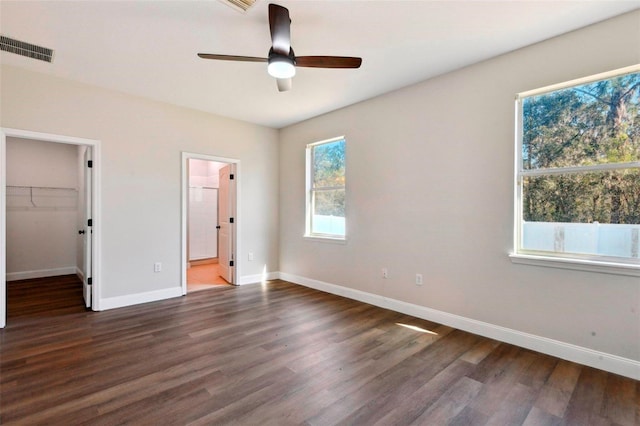 unfurnished bedroom featuring dark wood-type flooring, ensuite bath, a spacious closet, and ceiling fan