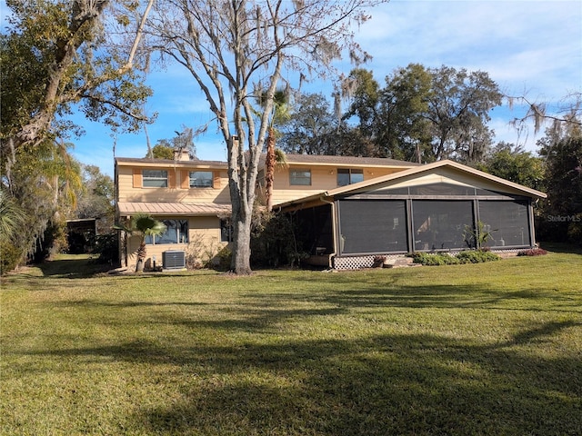 rear view of house featuring central AC unit, a sunroom, and a lawn