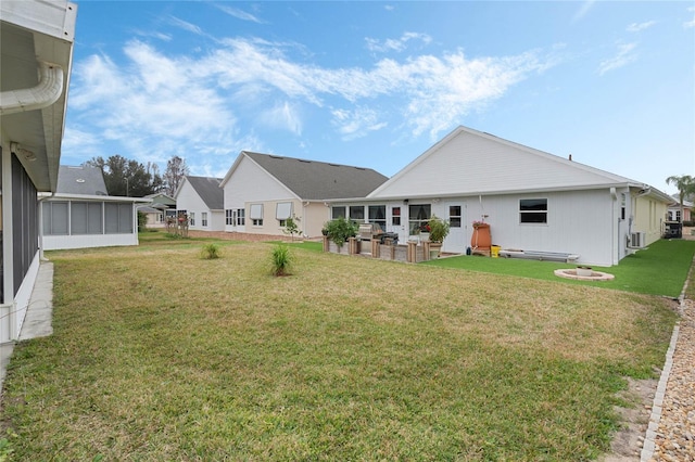 rear view of property with an outdoor fire pit, a sunroom, and a lawn