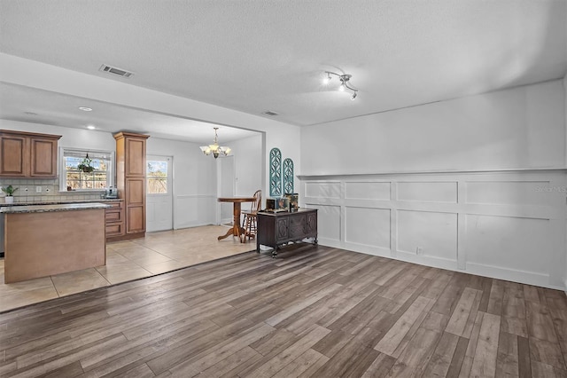 interior space with pendant lighting, tasteful backsplash, a chandelier, a textured ceiling, and light hardwood / wood-style flooring