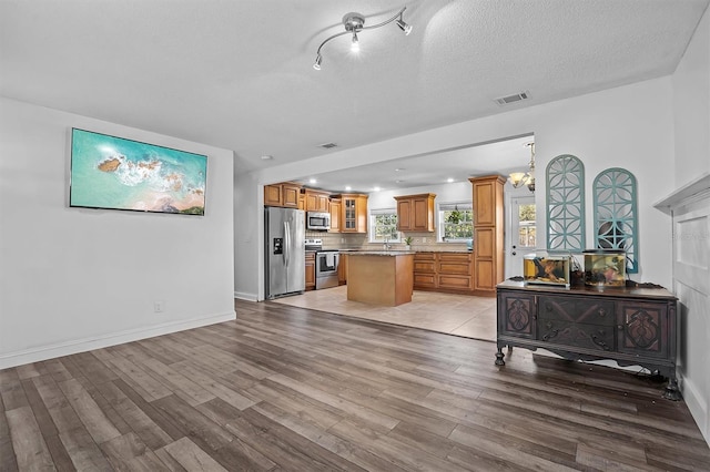 kitchen with appliances with stainless steel finishes, a center island, a textured ceiling, and light wood-type flooring