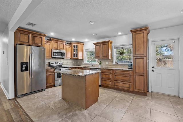 kitchen featuring sink, a center island, dark stone counters, stainless steel appliances, and decorative backsplash