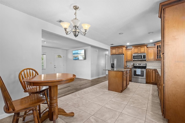 kitchen with a chandelier, a center island, light tile patterned floors, dark stone countertops, and appliances with stainless steel finishes