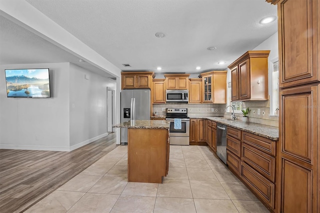 kitchen featuring a kitchen island, sink, backsplash, light stone counters, and stainless steel appliances