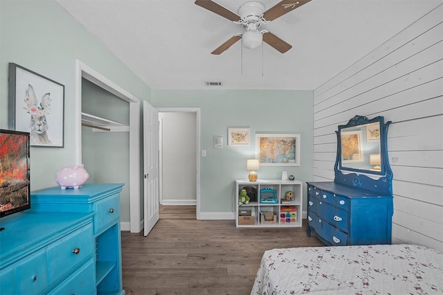 bedroom with dark hardwood / wood-style flooring, wooden walls, a closet, and ceiling fan