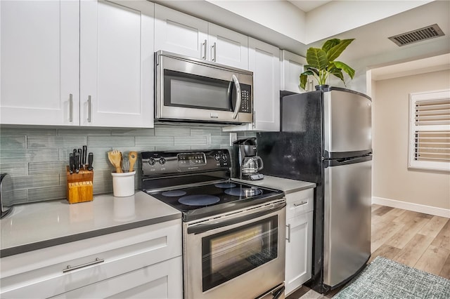 kitchen featuring appliances with stainless steel finishes, white cabinets, light wood-type flooring, and decorative backsplash