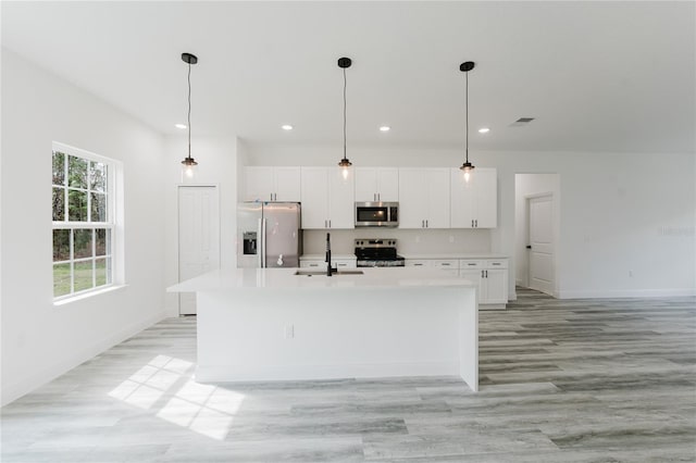 kitchen featuring sink, white cabinetry, decorative light fixtures, an island with sink, and stainless steel appliances