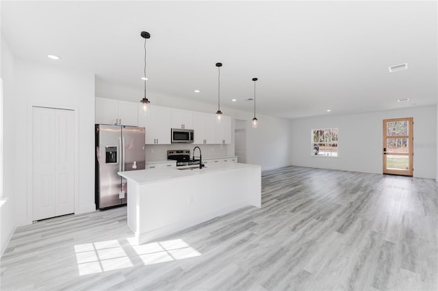 kitchen with sink, appliances with stainless steel finishes, pendant lighting, a kitchen island with sink, and white cabinets