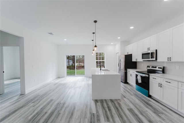 kitchen with appliances with stainless steel finishes, white cabinetry, sink, hanging light fixtures, and a kitchen island with sink