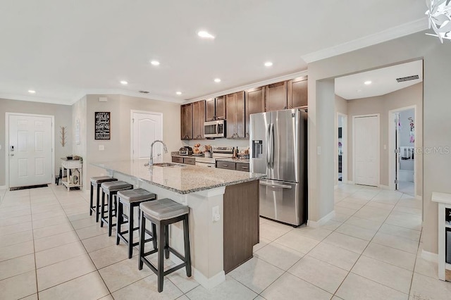 kitchen with light tile patterned flooring, appliances with stainless steel finishes, a kitchen bar, light stone countertops, and a center island with sink