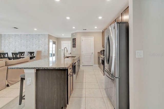 kitchen with light tile patterned flooring, a kitchen bar, sink, appliances with stainless steel finishes, and a kitchen island with sink