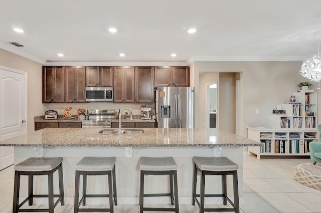 kitchen with a kitchen island with sink, sink, light stone countertops, and appliances with stainless steel finishes