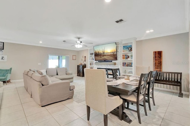 tiled dining room with crown molding, a stone fireplace, built in features, and ceiling fan