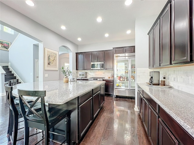 kitchen with stainless steel appliances, dark hardwood / wood-style flooring, light stone countertops, and a kitchen breakfast bar