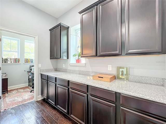 kitchen with dark hardwood / wood-style flooring, dark brown cabinets, and light stone countertops