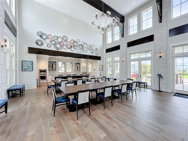 dining space featuring a towering ceiling, a notable chandelier, light hardwood / wood-style floors, and french doors